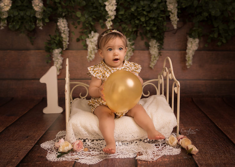 a baby girl just finished one sitting on the small bed with ballon