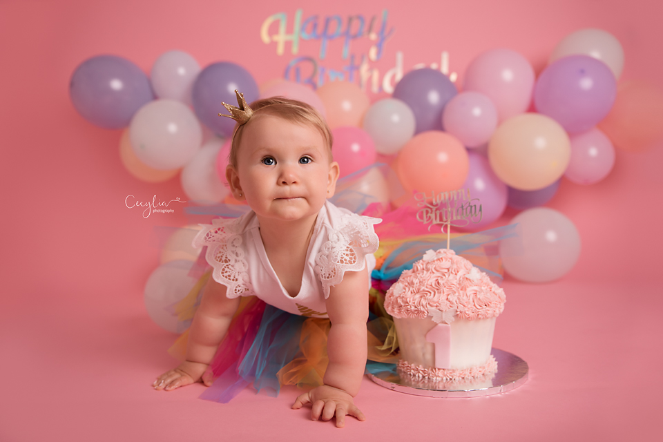 a baby on pink on her first birthday with a cake