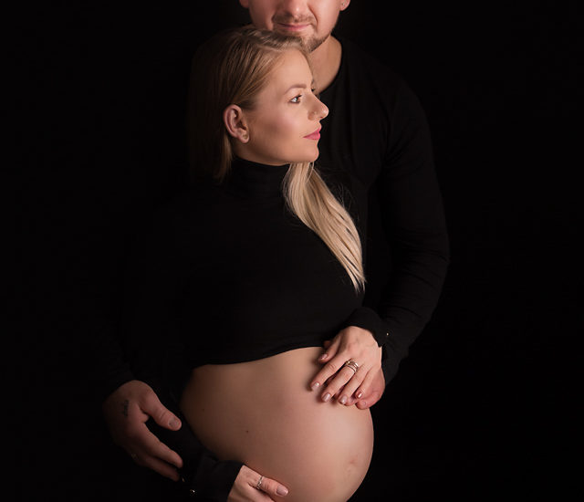 a couple expecting a baby having a maternity photo session done posing on the black background