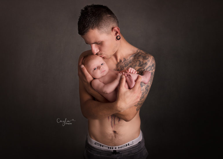 a daddy with tattoo holding a newborn
