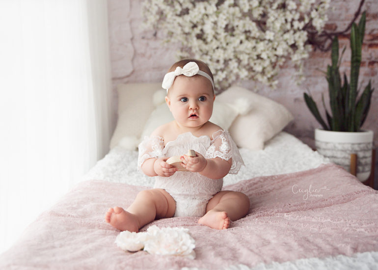 baby sitting on the bed in white dress