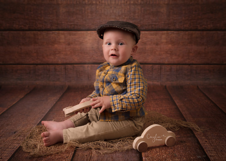 a baby boy sitting on the floor in wee hat playing wooden car