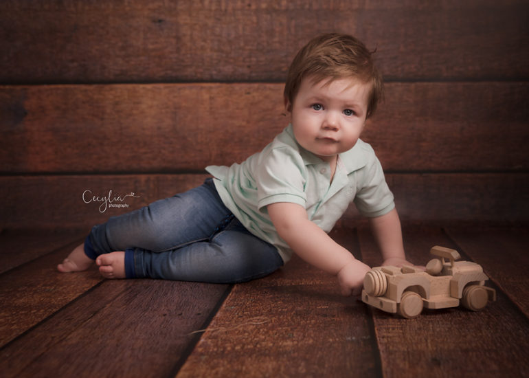 a baby boy sitting on the floor playing with wooden car toy