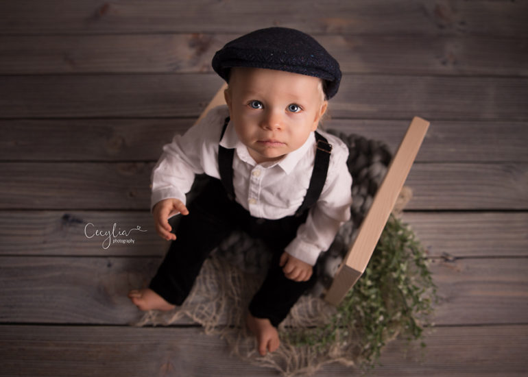a baby boy in black hat on the bed photo session