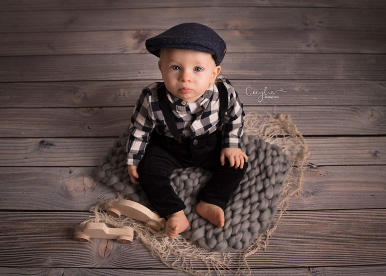 a baby boy with black hat sitting on the floor by best photographer